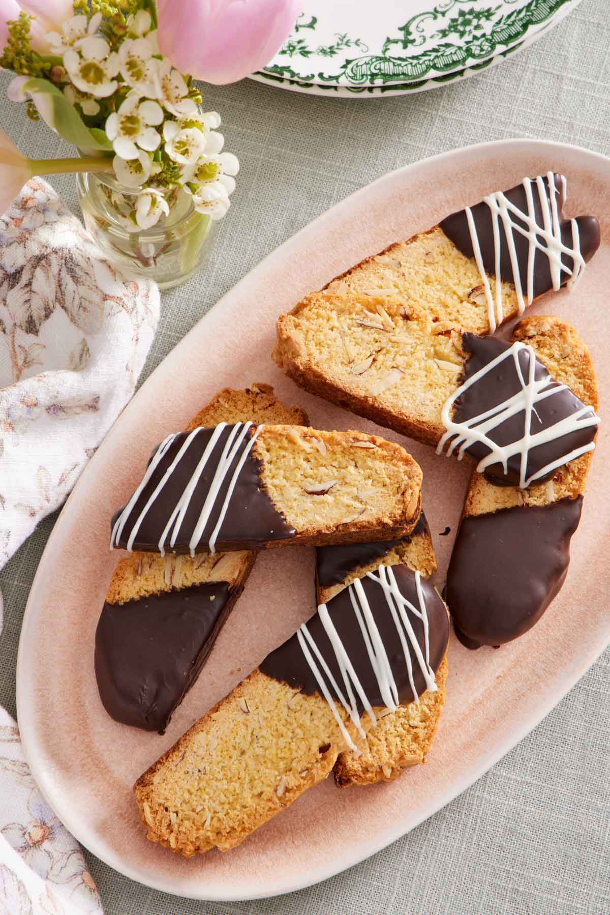 Overhead view of a platter of biscotti that are half dipped in chocolate with some with a drizzle of white chocolate on top.