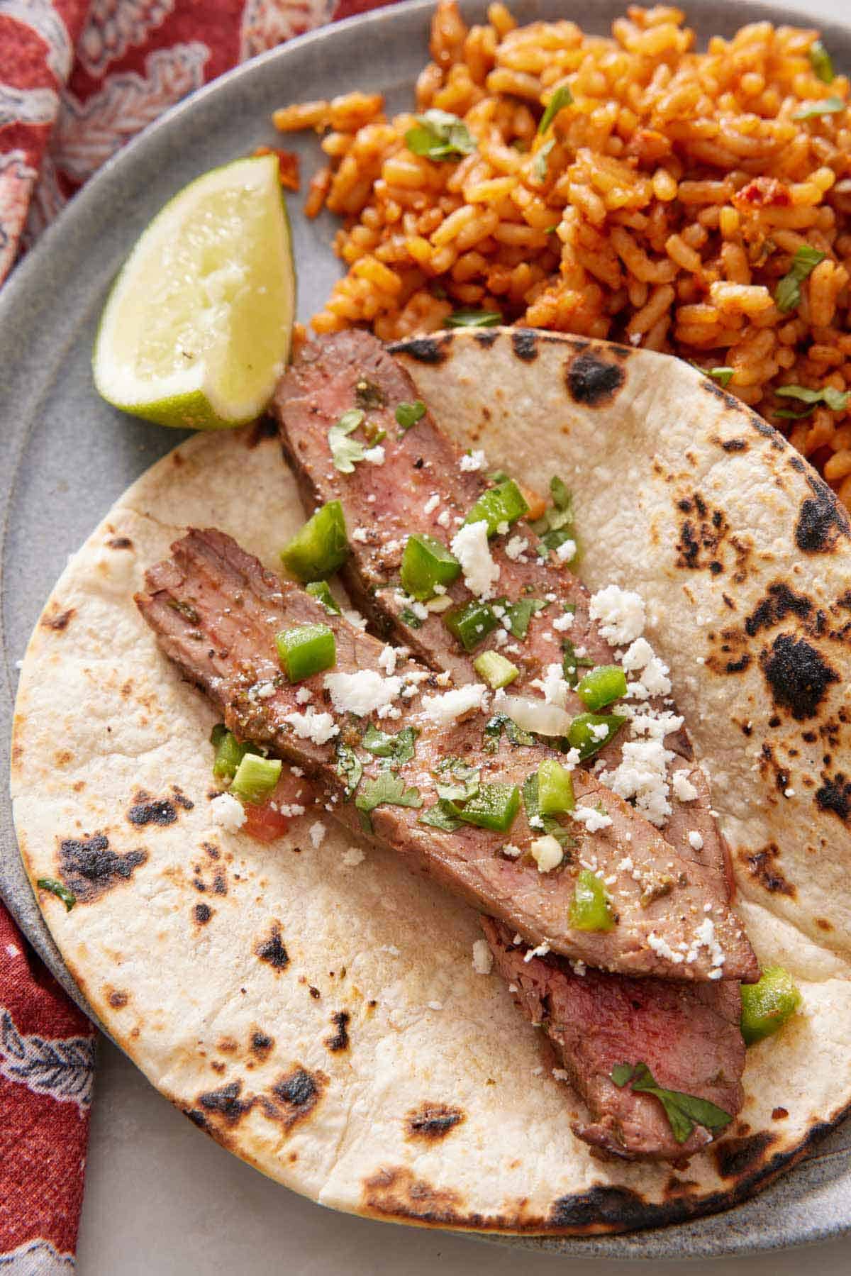 A plate with a tortilla with carne asada topped with crumbled cheese and cilantro. A lime and rice on the side.