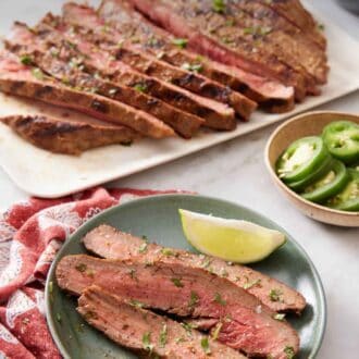 Pinterest graphic of a plate of carne asada with a lime wedge. A platter with the rest of the carne asada in the background also with tortillas, sliced jalapenos, and rice.