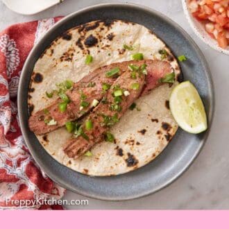 Pinterest graphic of a corn tortilla with sliced carne asada topped with chopped cilantro and a lime wedge.