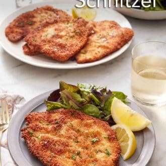 Pinterest graphic of a plate with a crispy chicken schnitzel, mixed greens, and lemon wedges. A drink in the back along with a platter with more chicken schnitzels.