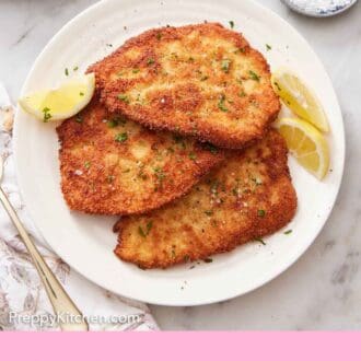 Pinterest graphic of a platter of chicken schnitzel with lemon wedges. A bowl of salt on the side.