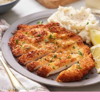 Pinterest graphic of a sliced chicken schnitzel on a plate with lemon wedges and mashed potatoes.