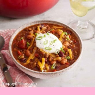 Pinterest graphic of a bowl of chili topped with sour cream, green onions, and shredded cheese.