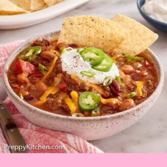 Pinterest graphic of a bowl of chili with sliced jalapeno, sour cream, and shredded cheese with a tortilla chip tucked in.