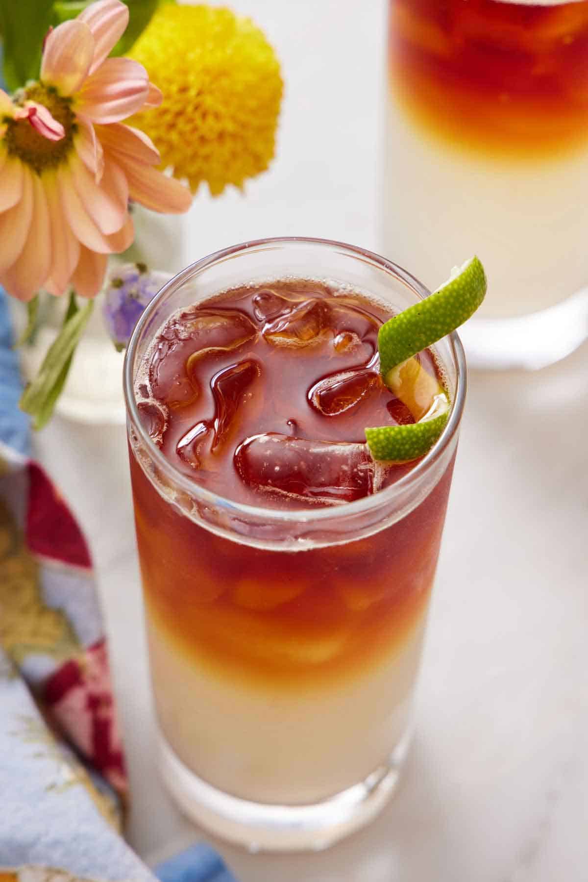 A glass of Dark and Stormy with a lime zest garnish with some flowers on the side.