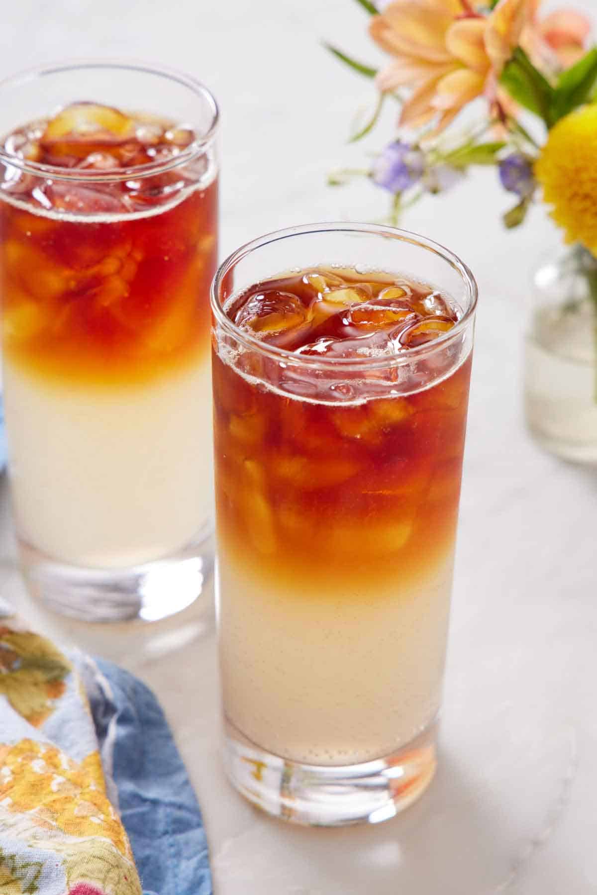 Two glasses of Dark and Stormy before stirring. A vase of flowers in the background.