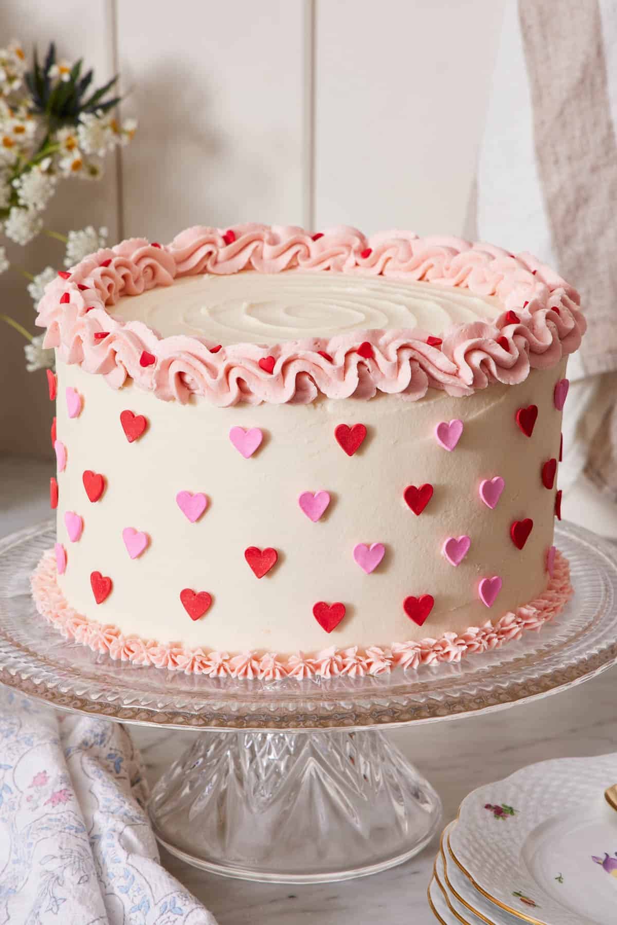 A cake on a cake stand with pink piping and heart sprinkles.