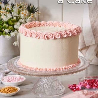 Pinterest graphic of a cake with white frosting and pink frosting piped on the top and bottom of the cake on a cake stand. A piping bag and bowls of sprinkles on the counter.