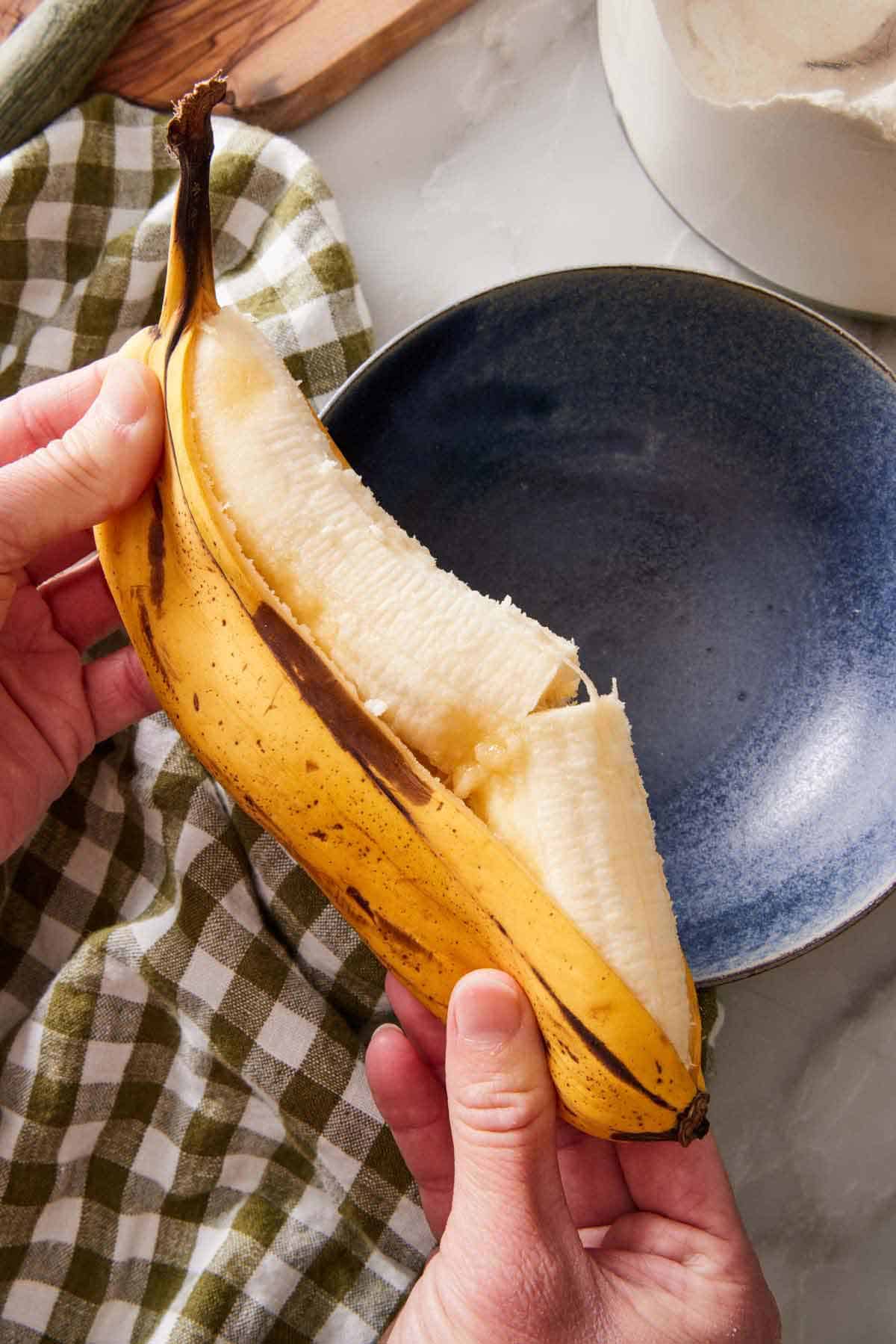 A ripened banana partially peeled and being squeezed out into a bowl.