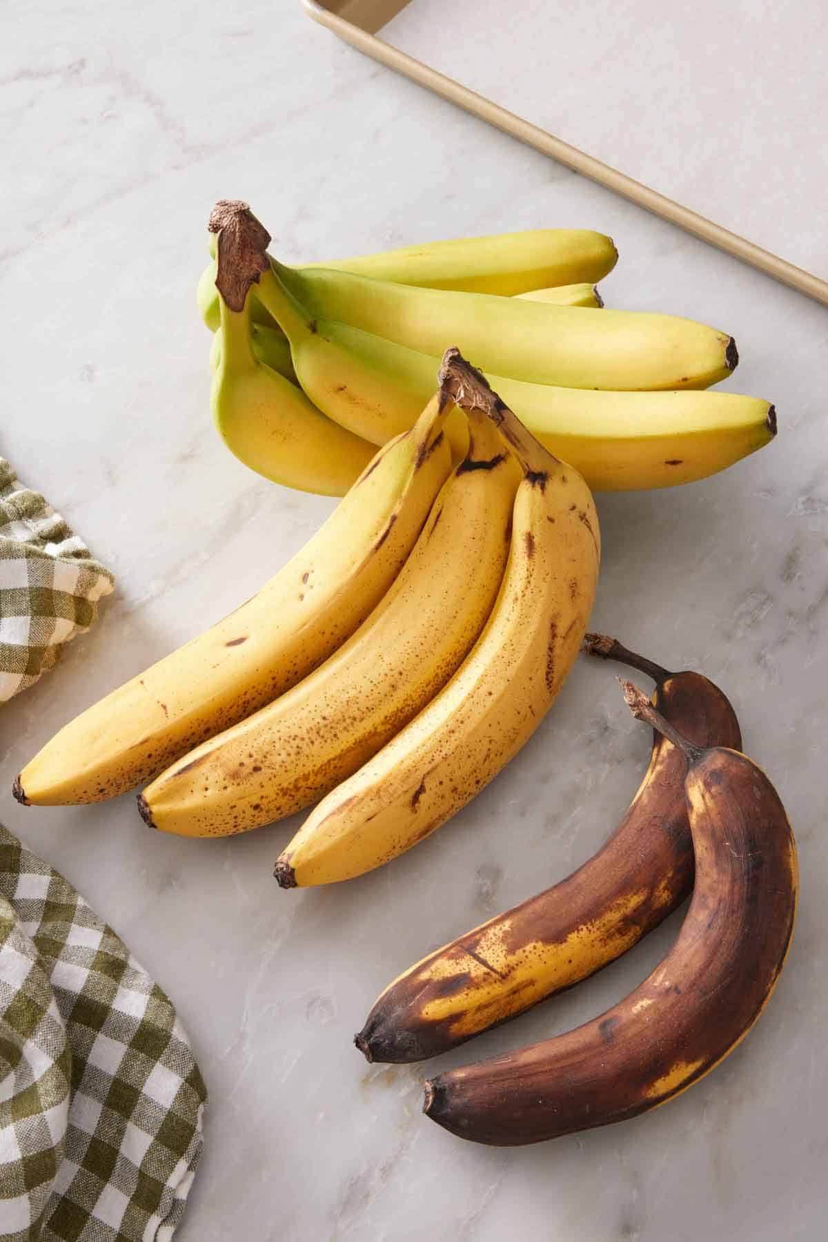 Three bundles of bananas, one slightly green, one spotty brown, and one super ripe.