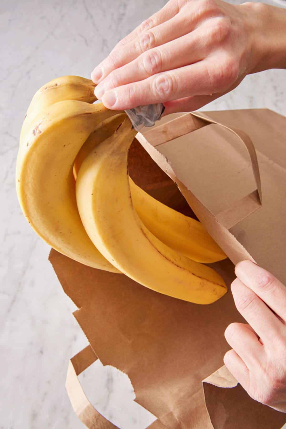 A bundle of bananas placed into a brown paper bag.