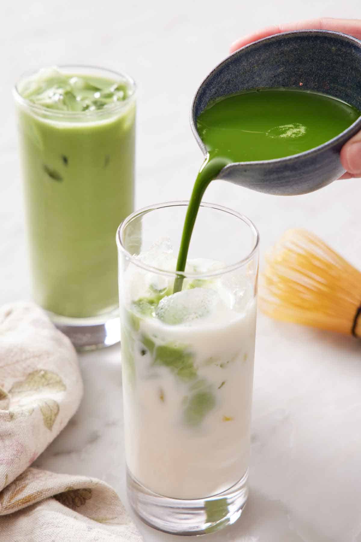 Matcha poured into a glass with milk and ice. Another iced matcha latte in the background.