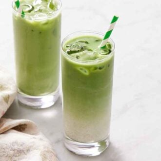 Two iced matcha lattes with straws with a napkin on the side.