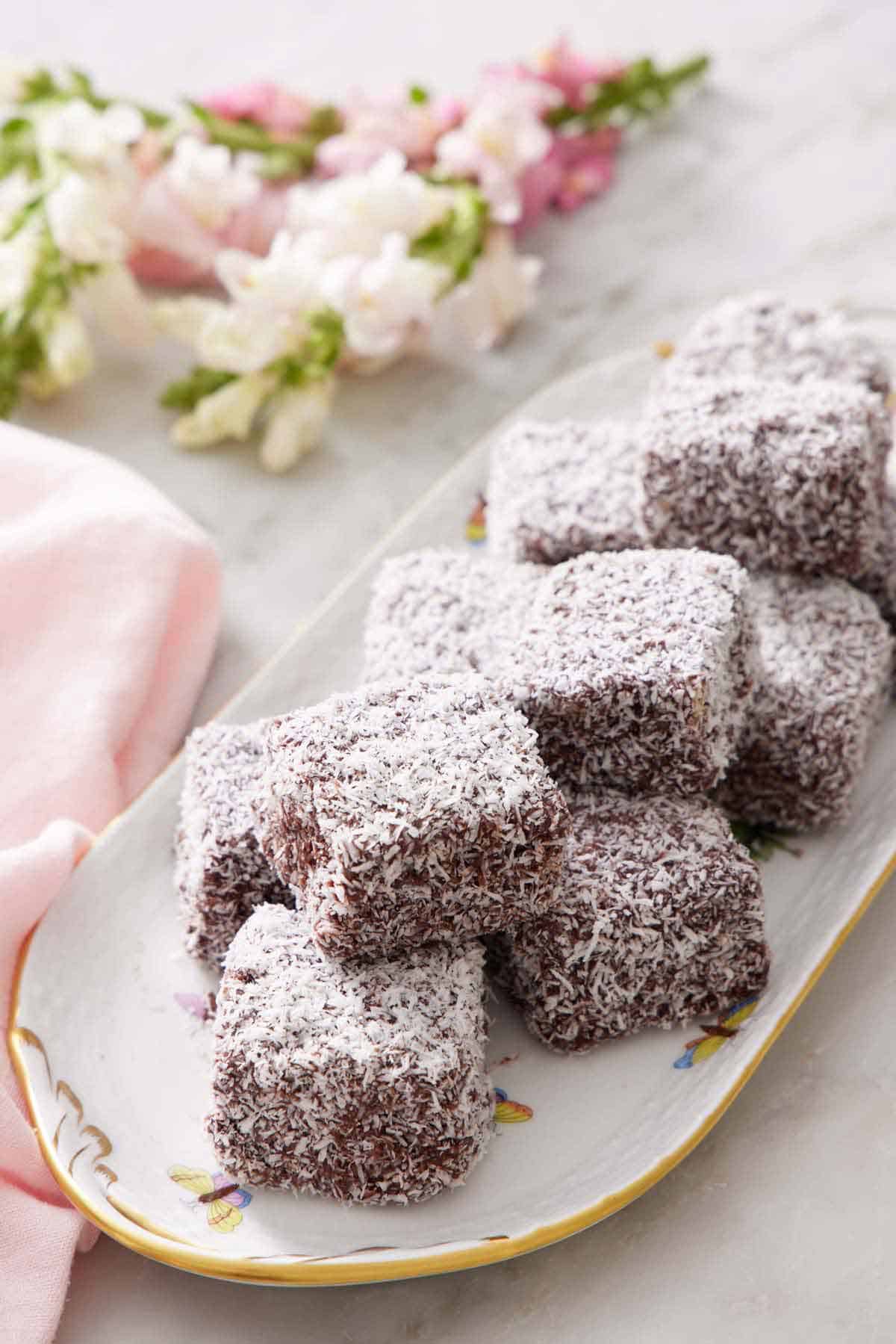 A platter of lamingtons with flowers in the background.