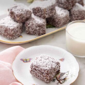 Pinterest graphic of a plate with a lamington with a glass of milk and platter of more lamingtons.