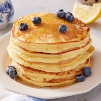 A stack of lemon ricotta pancakes with fresh blueberries and maple syrup on top.