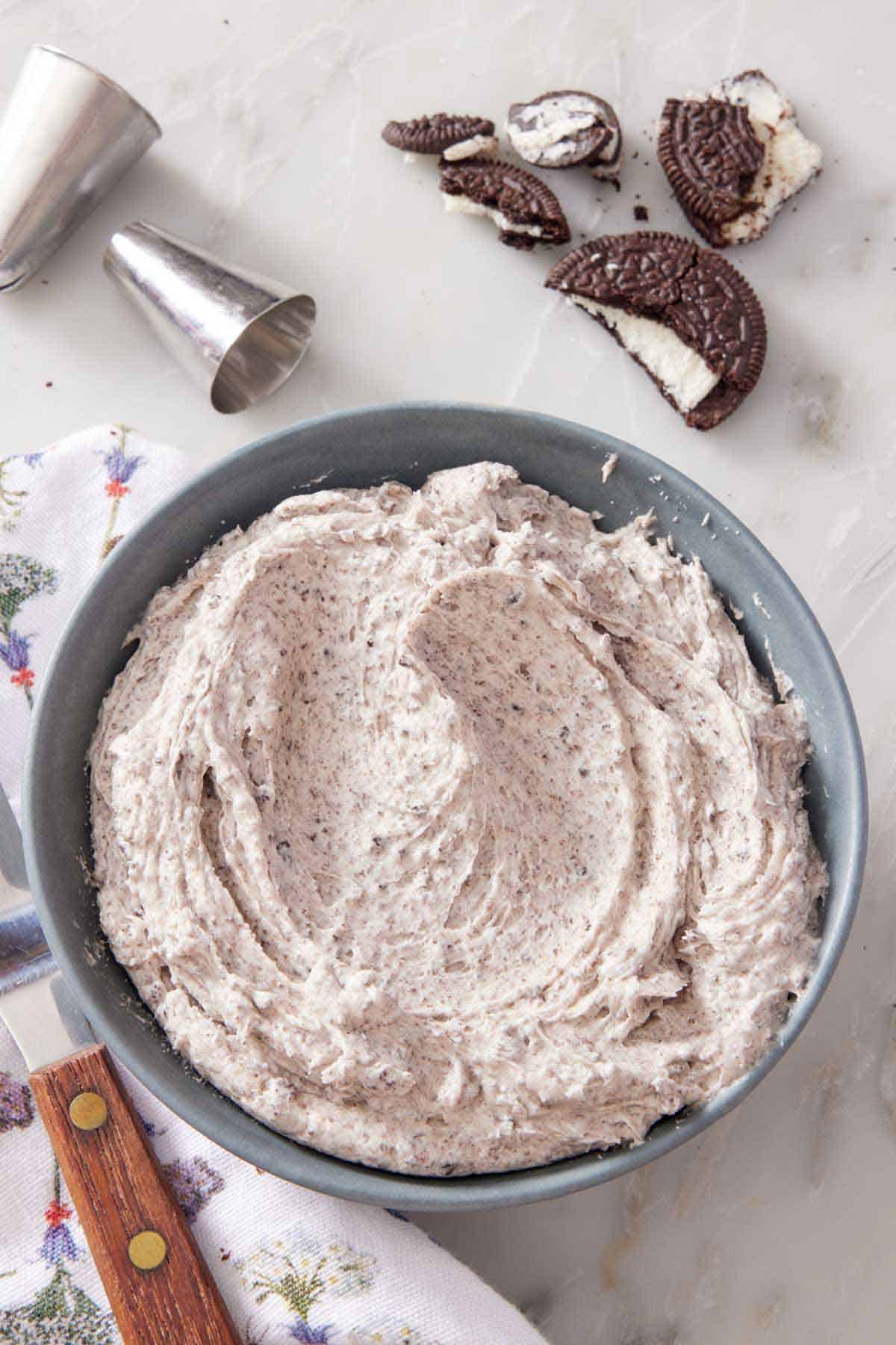 Overhead view of a bowl of Oreo frosting. Some piping tips and broken Oreo cookies off to the side.