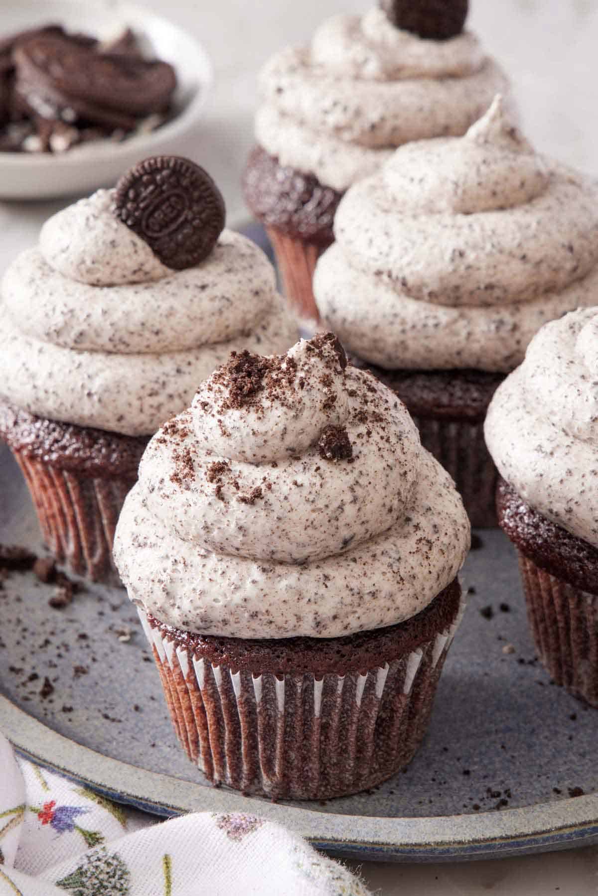 A platter of multiple cupcakes topped with Oreo frosting. One cupcake with Oreo crumbles on top and another with a mini Oreo.