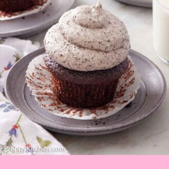 Pinterest graphic of a chocolate cupcake topped with Oreo frosting on a plate with the paper lining pulled down. More cupcakes in the background and a glass of milk.