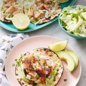 Pinterest graphic of a plate with an open faced salmon taco with a lime wedge and avocado on the side. More tacos in the background.