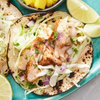 A close up view of salmon tacos on a platter with some cut limes around.