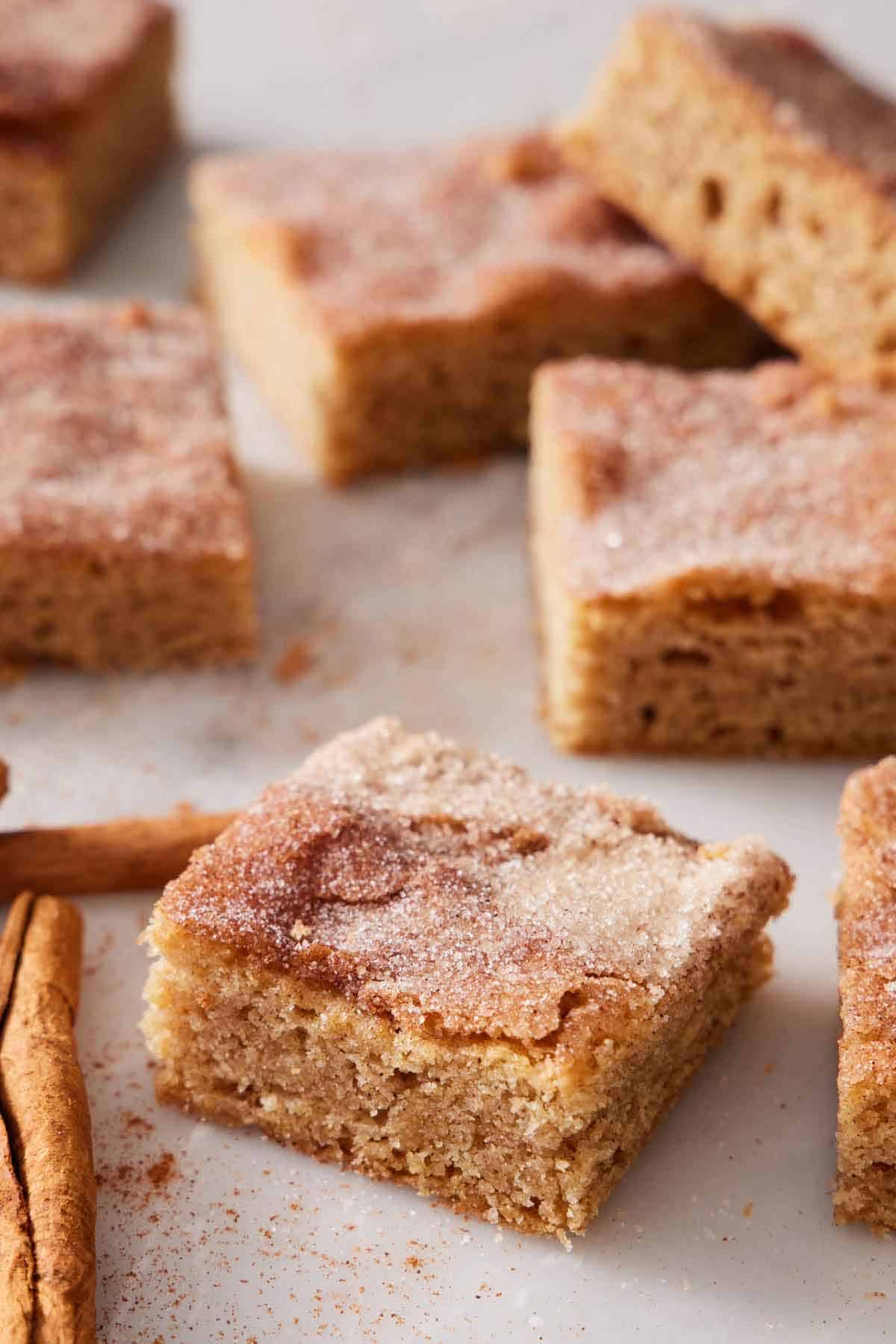 Sliced snickerdoodle bars on a marble surface with cinnamon sugar dusted all around.