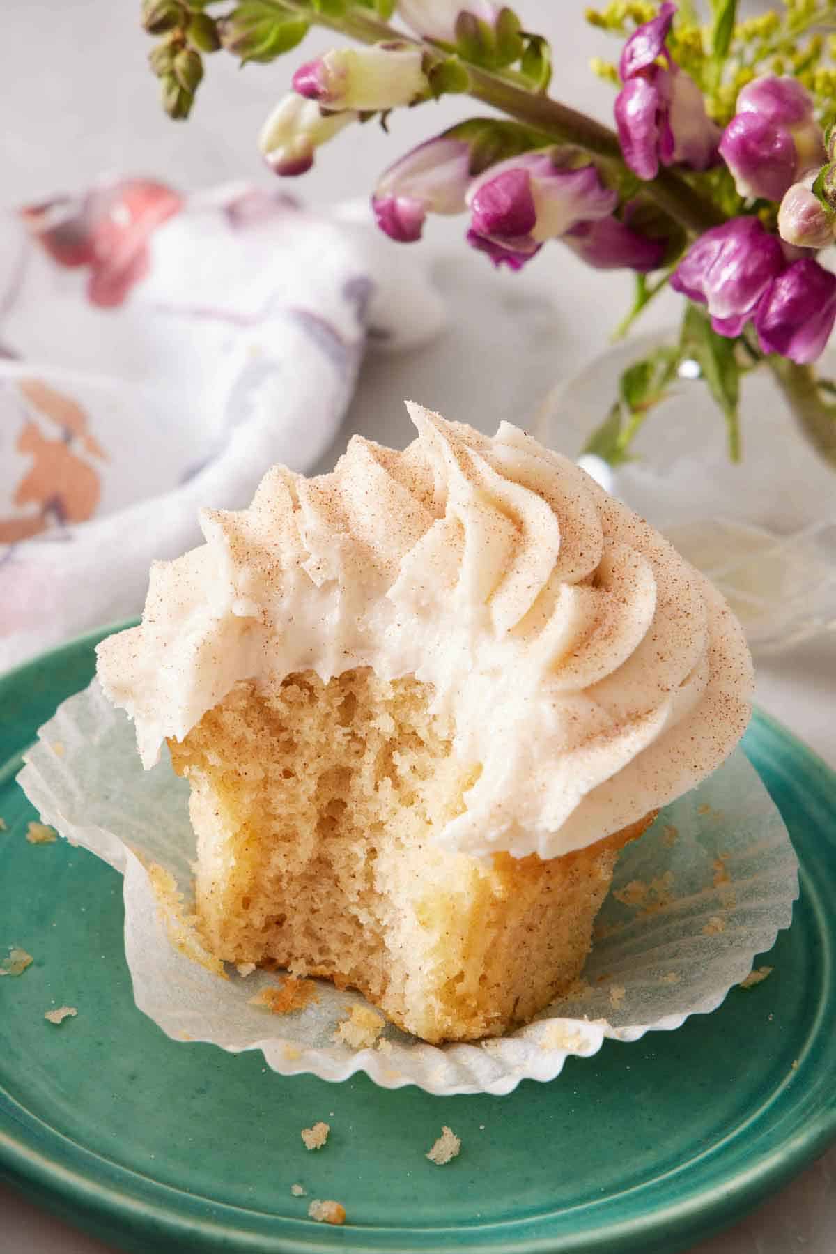 A plate with a snickerdoodle cupcake with the liner peeled down and a bite taken out of it.