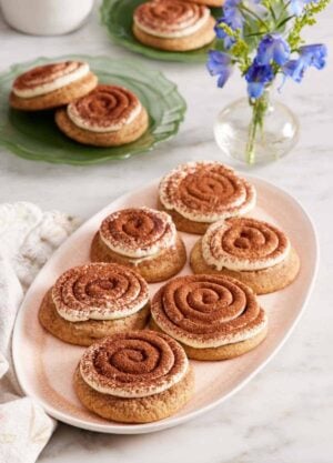 A platter of tiramisu cookies with a vase of flowers and two more plates of tiramisu cookies in the background.