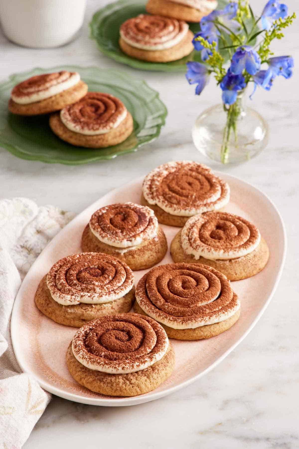 A platter of tiramisu cookies with a vase of flowers and two more plates of tiramisu cookies in the background.