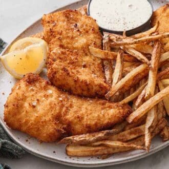 A platter with air fryer fish and chips with a bowl of tartar sauce and lemon wedges. A napkin on the side.