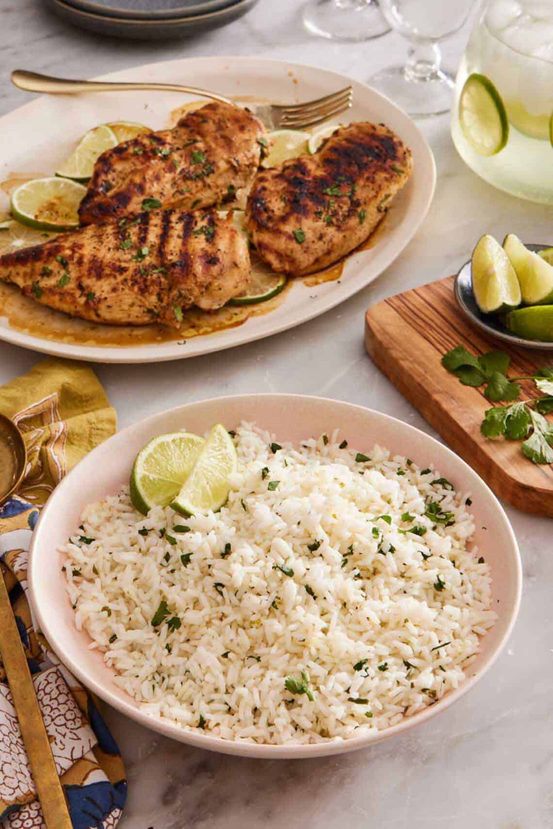 A bowl of cilantro lime rice with grilled chicken in the background. Cut limes and cilantro on the side.