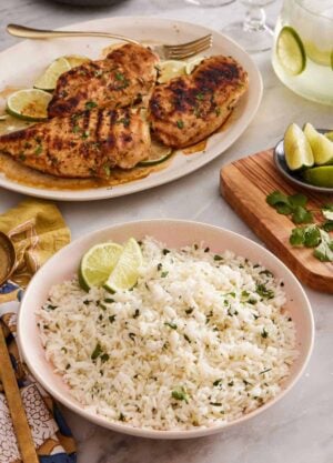 A bowl of cilantro lime rice with grilled chicken in the background. Cut limes and cilantro on the side.