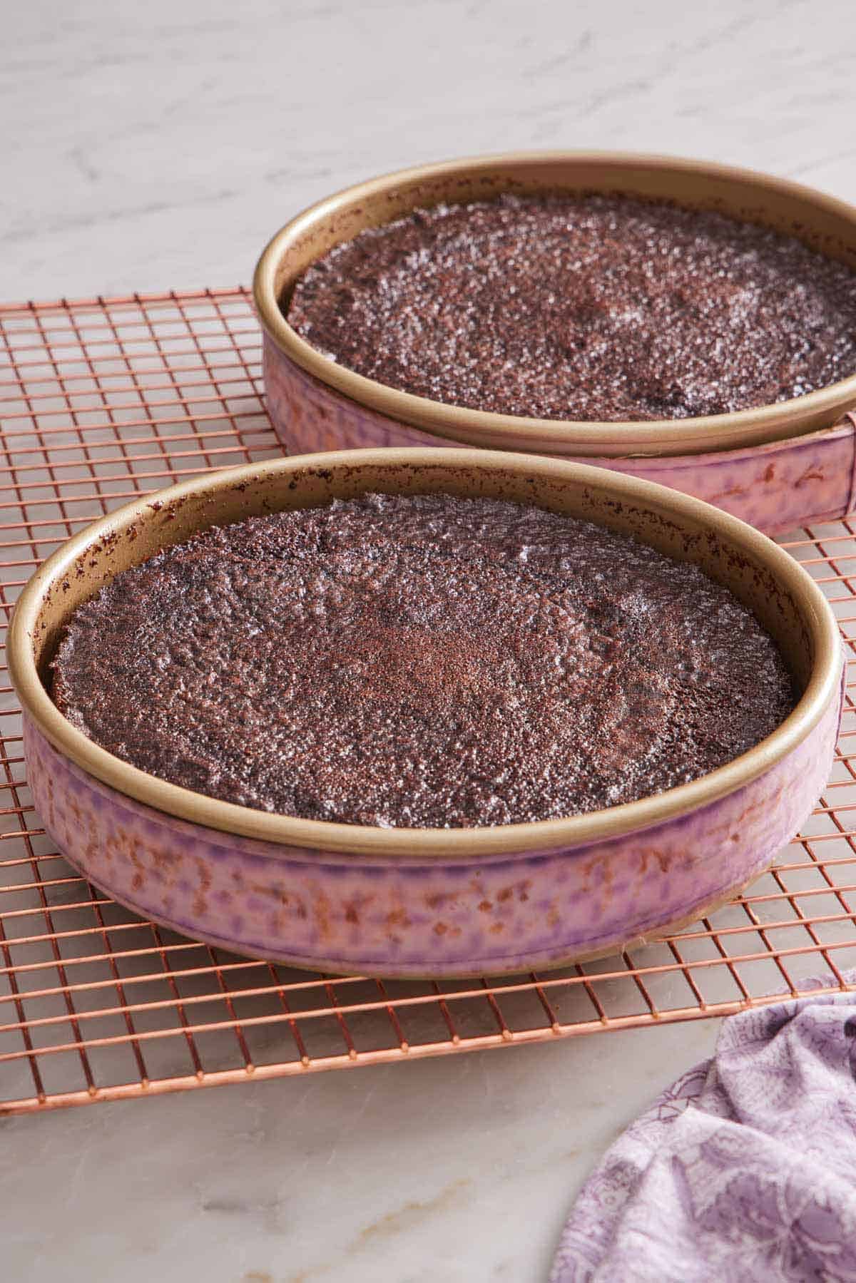 Two baking pans of perfectly baked cake layers in baking pans wrapped in fabric cake strips on a cooling rack.