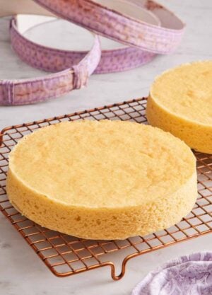 A cooling rack with two cakes with perfectly flat tops. Fabric cake strips in the background.