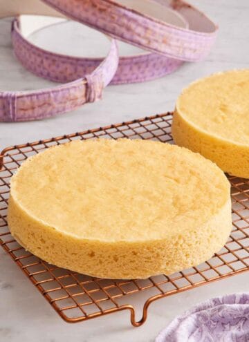 A cooling rack with two cakes with perfectly flat tops. Fabric cake strips in the background.