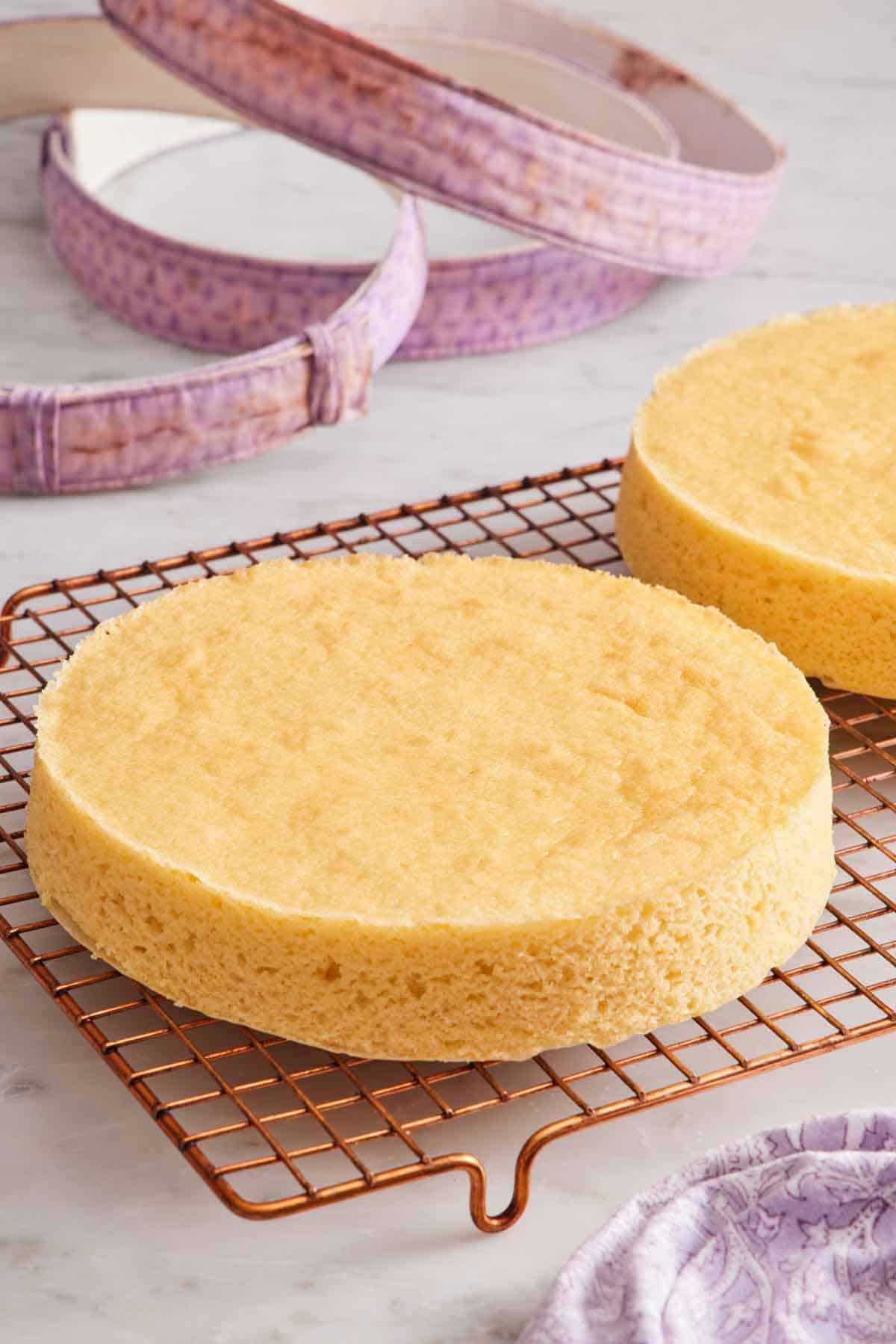 A cooling rack with two cakes with perfectly flat tops. Fabric cake strips in the background.