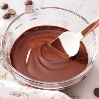 A bowl of melted chocolate with a spatula inside. Chocolate chips scattered around and a linen napkin beside the bowl.