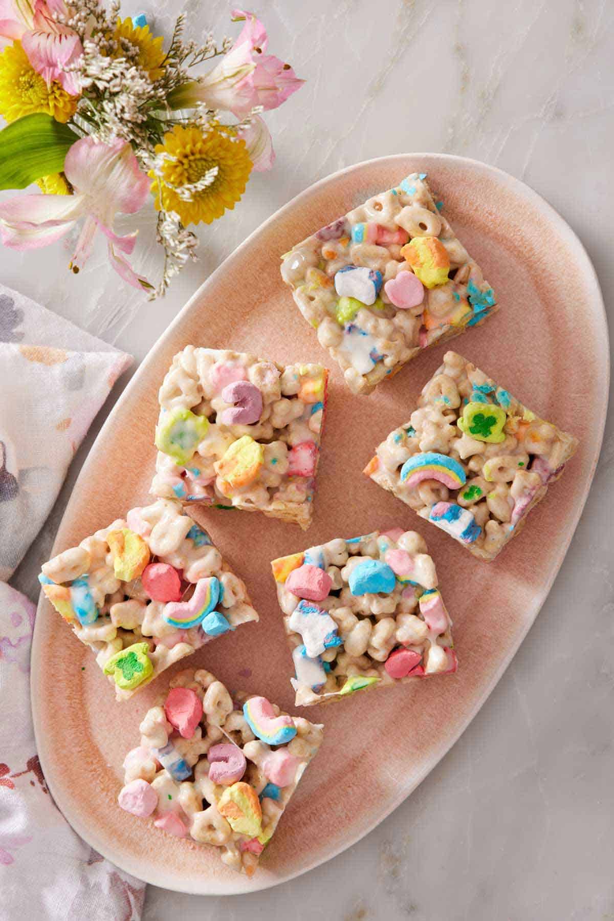 Overhead view of six pieces of Lucky Charms treats on an oval platter. Flowers off to the side.