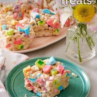 Pinterest graphic of a square piece of Lucky Charms treat on a plate. A platter with more Lucky Charms treats in the background along with a vase of flowers.