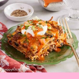 Pinterest graphic of a plate with a serving of Mexican lasagna with a dollop of sour cream and hot sauce on top with chopped tomatoes and green onions.