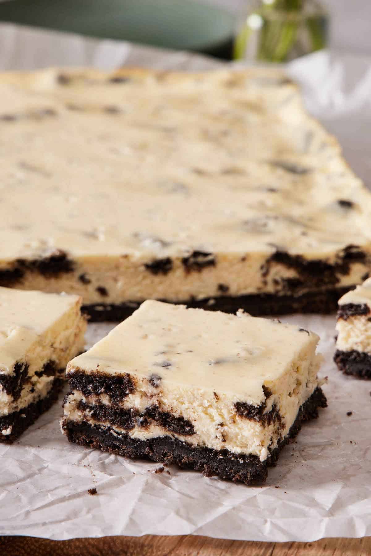 Cut Oreo cheesecake bars on a parchment-lined wooden serving board.