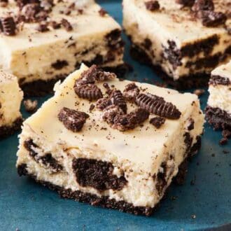 Oreo cheesecake bars on a blue platter with crushed oreos on top.