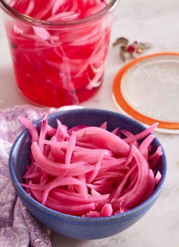 A bowl of pickled onions with a weck jar with the lid off in the background with more.