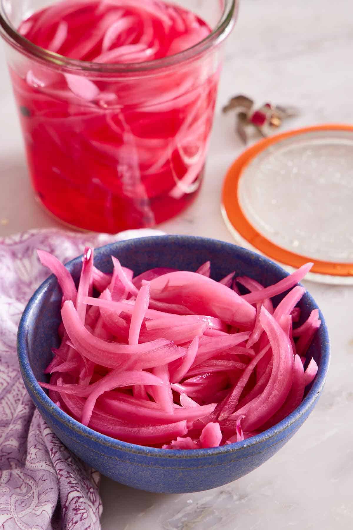 A bowl of pickled onions with a weck jar with the lid off in the background with more.