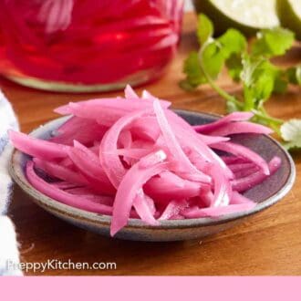 Pinterest graphic of a plate of pickled onions on a wooden serving board with a jar of more pickled onions in the background with some cilantro and limes.