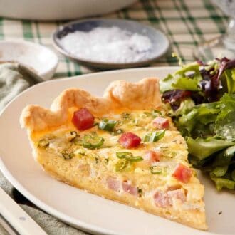 Pinterest graphic of a close up view of a slice of quiche with salad on the side.