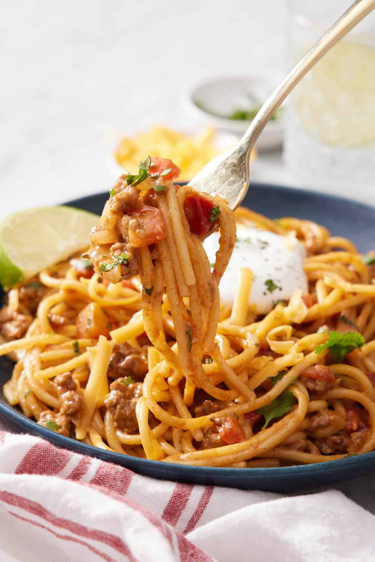 A fork lifting up some taco spaghetti from a bowl.