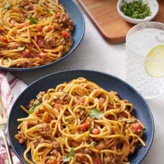 Pinterest graphic of two bowls of taco spaghetti with a drink, bowl of chopped cilantro, and two sauces in the background.