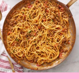 Pinterest graphic of a skillet of taco spaghetti. A stack of plates, forks, cilantro, and sour cream on the side.